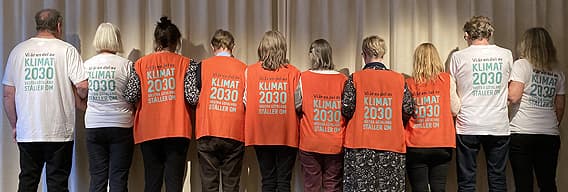Tio personer bakifrån som krokar arm med varsin tröja eller väst med Klimat 2030-tryck
