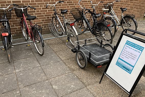 En fylld cykelparkering bakom en trottoarpratare med texten Cykling är en god idé