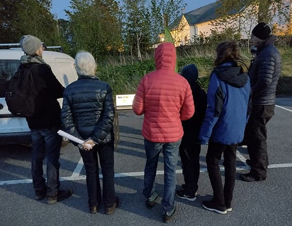 Deltagarna står utomhus runt en dator på ett bord