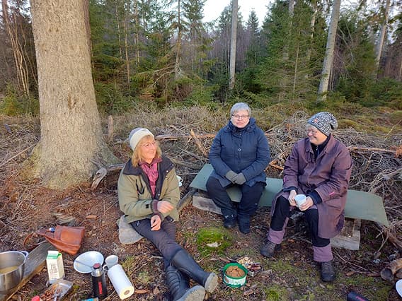 Tre deltagare fikar framför en skog
