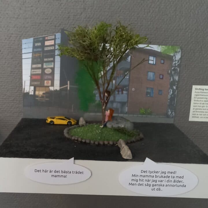 Miniatyr av en vuxen och ett barn som klättrar i ett träd mitt på en parkering med hus omkring. ...